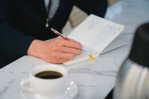 A Man Writing With A Cup Of Coffee Next To Him